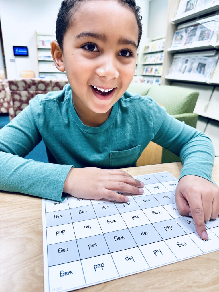 A young boy reading a CVC fluency grid.